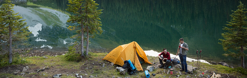 Two people camping next to a lake.