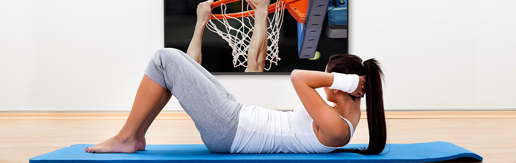 A woman performing a crunch while watching college basketball.