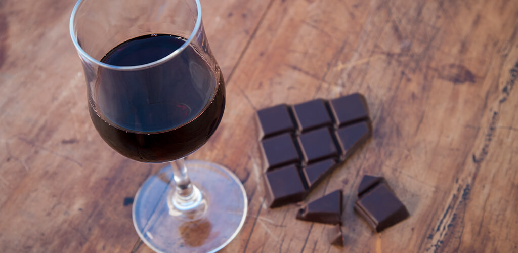 Dark chocolat next to a glass of red wine.